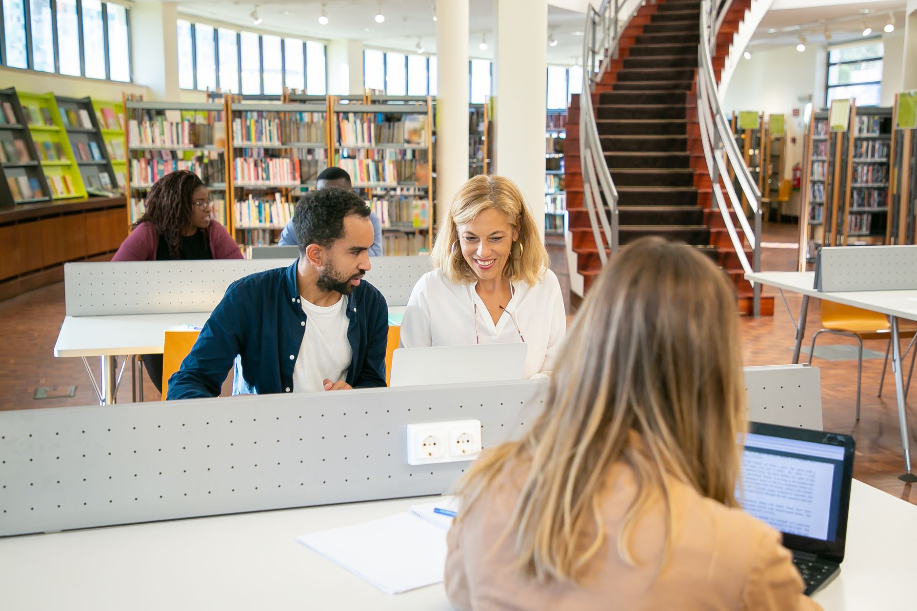 People sitting at a table in the library smiling, talking, and working.